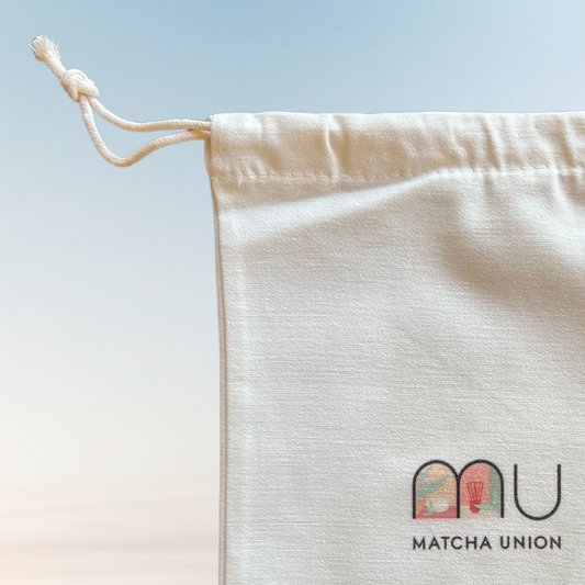 Close-up of the Matcha Union gift bag showing its cream cotton texture, drawstring closure and printed logo.
