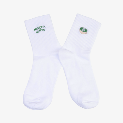 Pair of white ribbed Matcha Union socks with green embroidered brand lettering on one sock and a matcha cup design on the other.