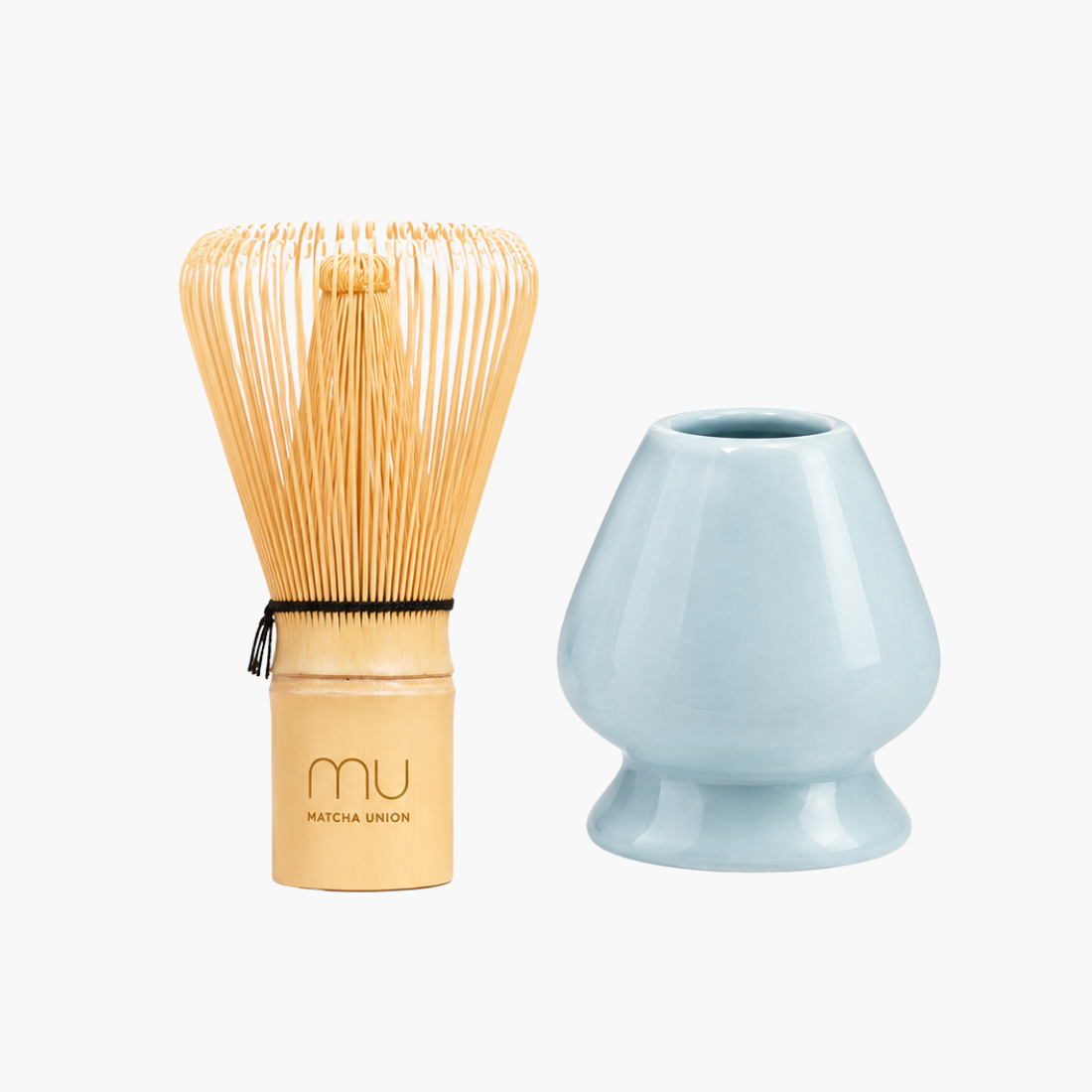 Matcha Union logo-engraved bamboo whisk beside a blue glazed ceramic holder, shaped to support the whisk’s prongs while drying.